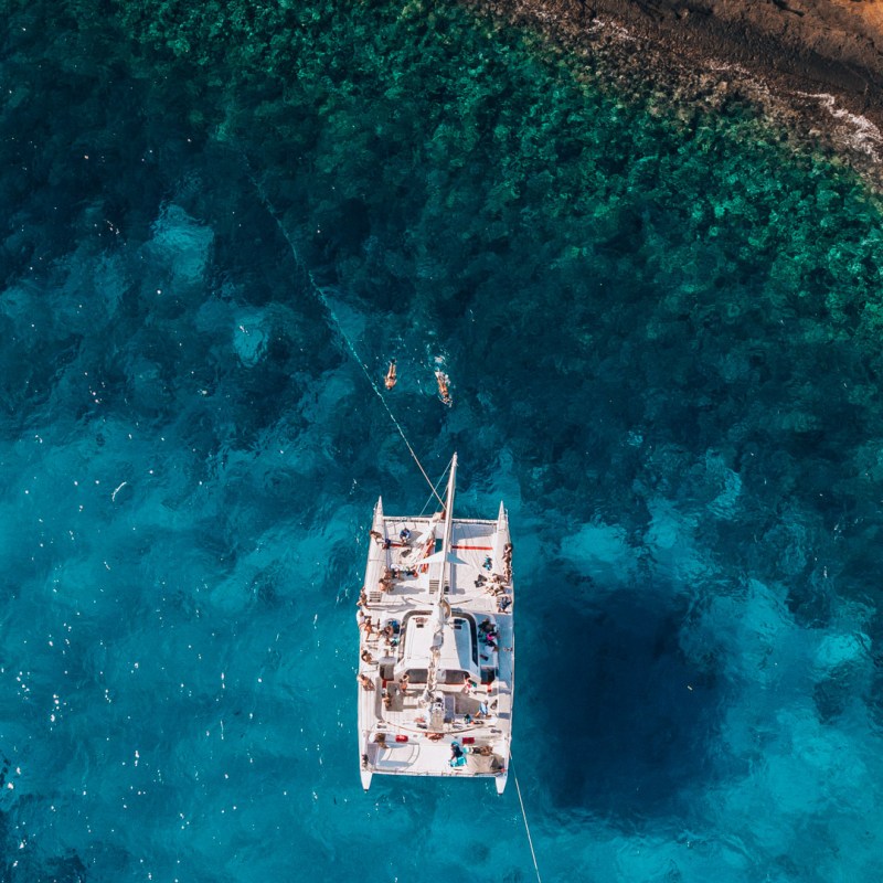 Aerial view of a boat on clear blue water near rocky shoreline.