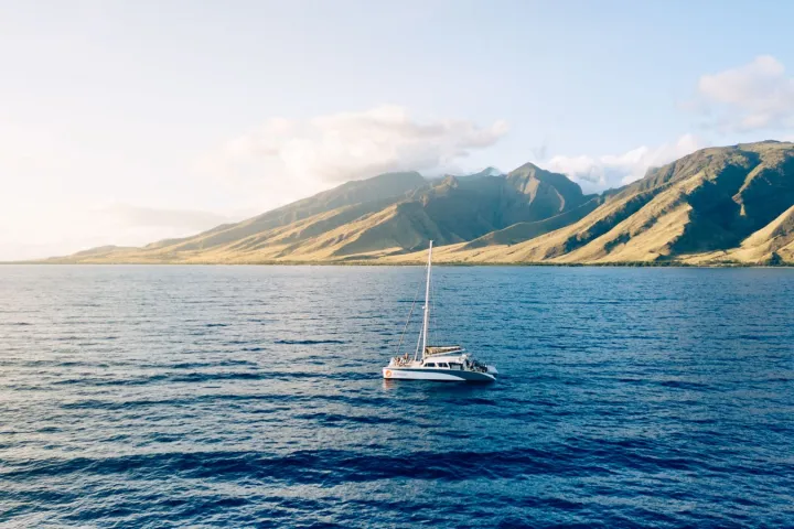 Sailboat on blue ocean with mountainous coastline under a clear sky.