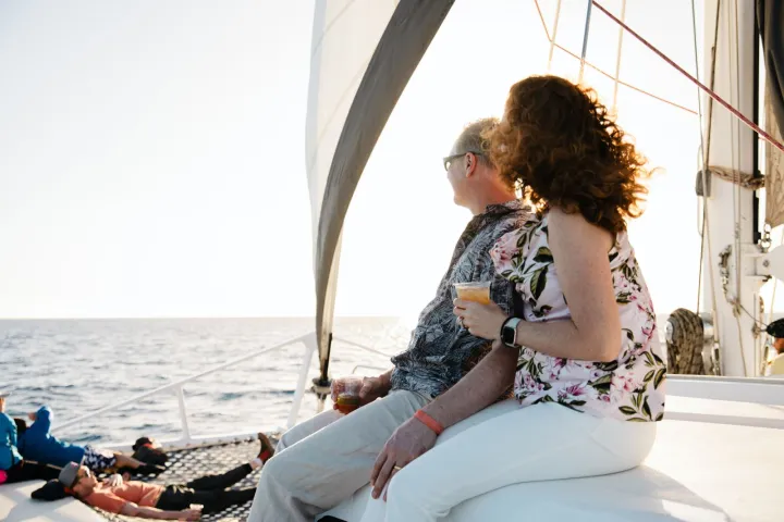 People relaxing on a sailboat, sitting and reclining, with drinks and ocean backdrop.