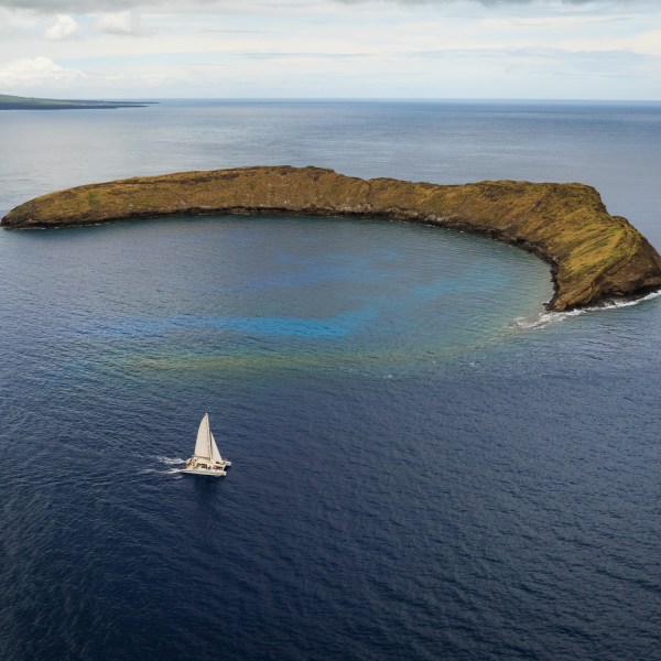 Sailboat near crescent-shaped island in blue ocean