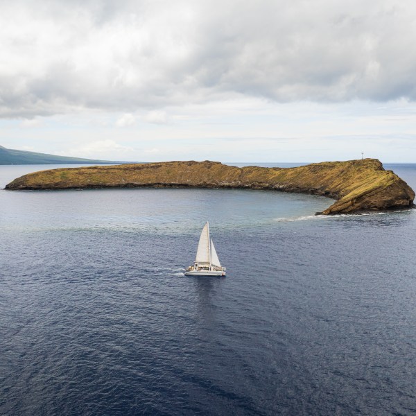 Sailboat near crescent-shaped island under cloudy sky.