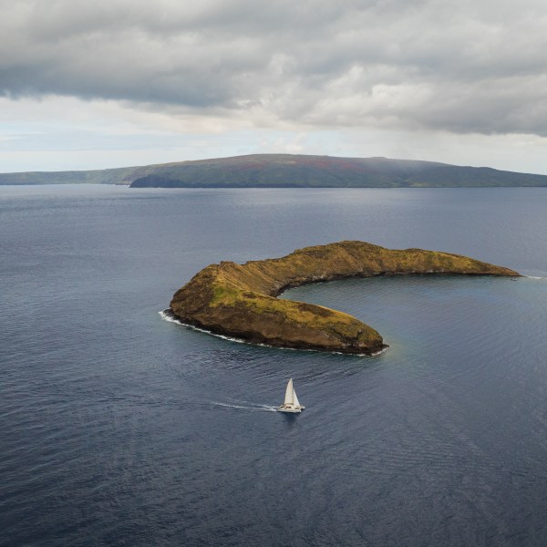 Boat sailing near crescent-shaped island surrounded by ocean under cloudy sky.