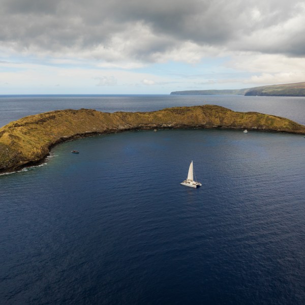 Sailboat near a crescent-shaped island under cloudy skies.