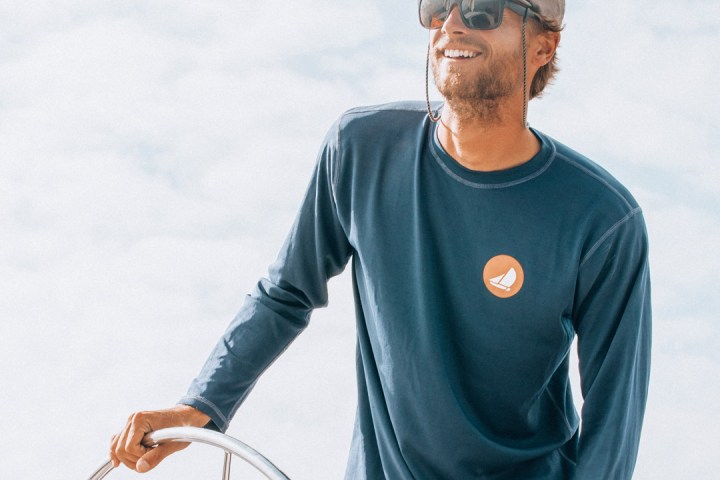 Man in blue shirt steering a sailboat on a sunny day.
