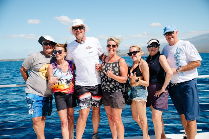 Seven people smiling on a boat with an ocean and blue sky backdrop.