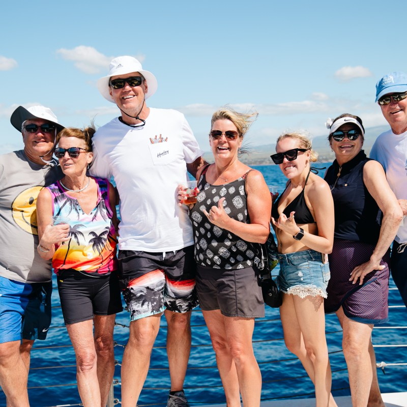 Seven people smiling on a boat with an ocean and blue sky backdrop.