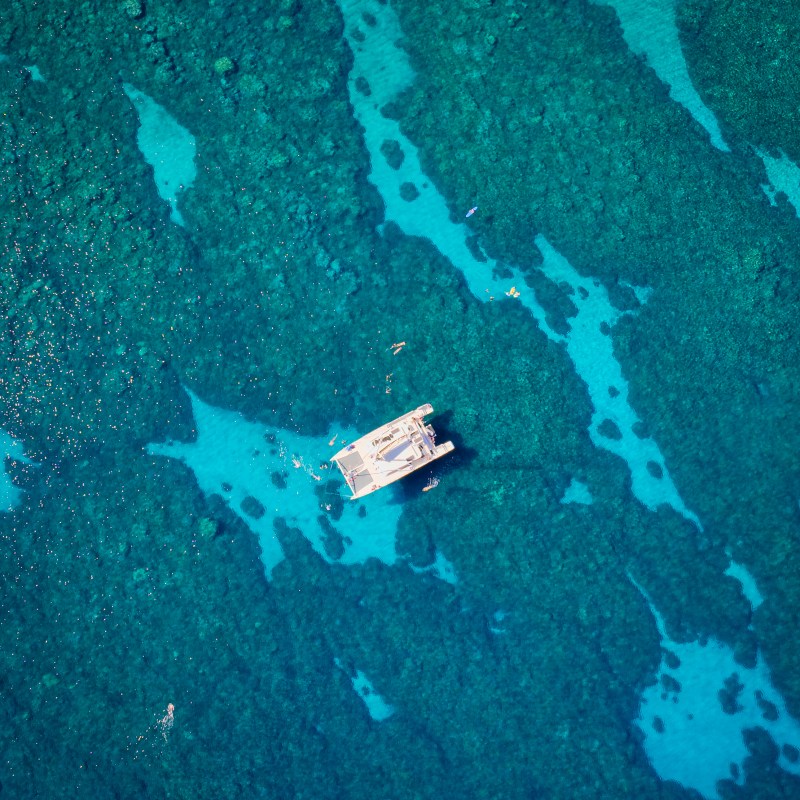 Aerial view of a boat on turquoise ocean over a coral reef with visible swimmers.