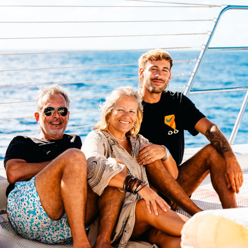 Three people sitting on a boat deck with the ocean in the background.