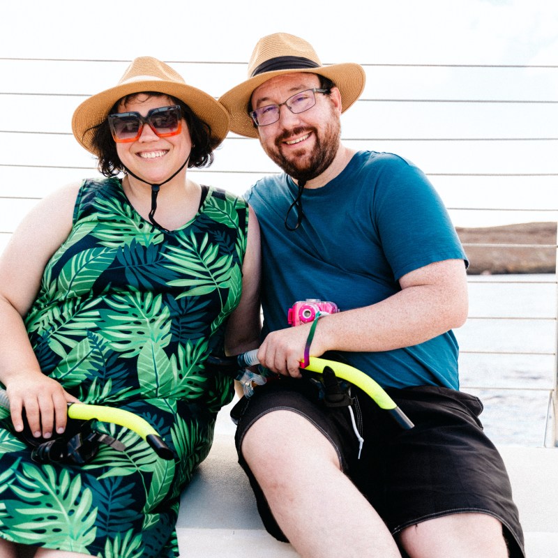 Two people wearing hats sitting on a boat, holding snorkeling gear.