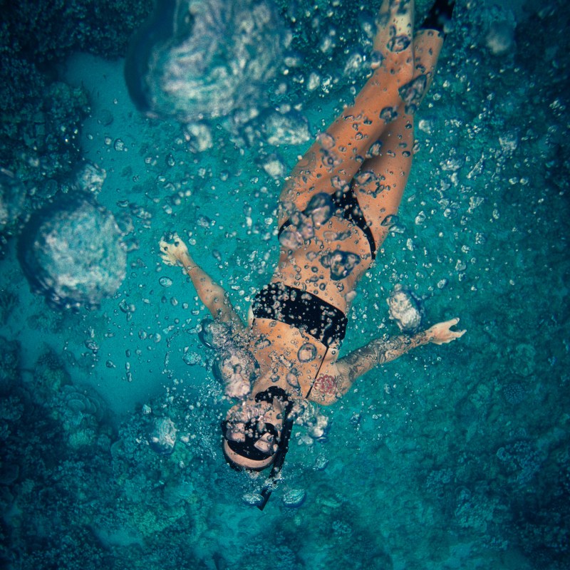 Person snorkeling underwater, surrounded by bubbles in clear blue water.