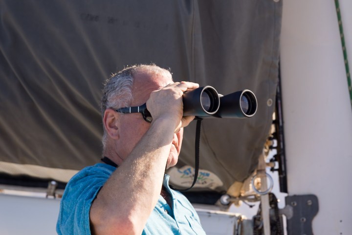 Man in blue shirt looking through binoculars on a boat.