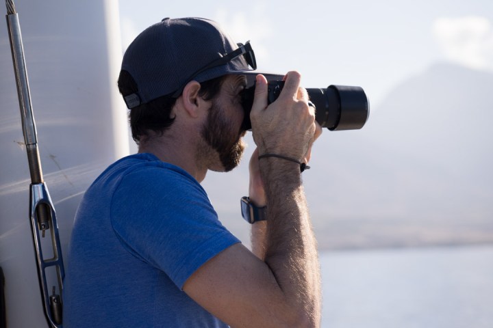 Man in blue shirt taking a photo with a DSLR camera on a boat.