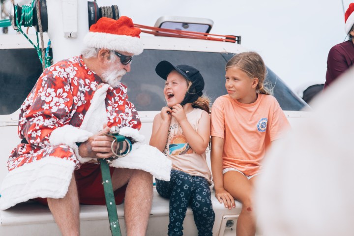 Man in a Santa suit sits with two smiling children on a boat.