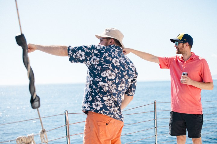 Two men on a boat pointing and looking at the ocean.