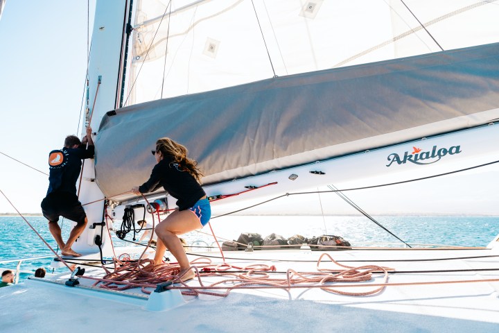 Two people adjusting sails on a boat named Akialoa in bright sunlight.