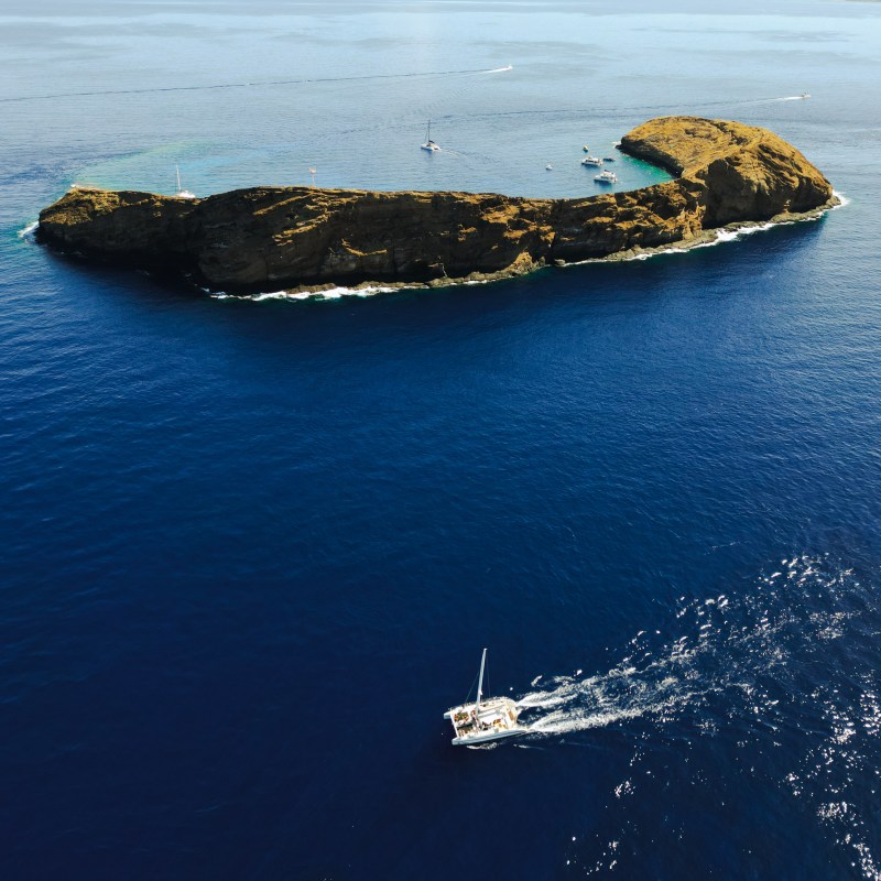 Aerial view of a small island with boats in blue ocean.