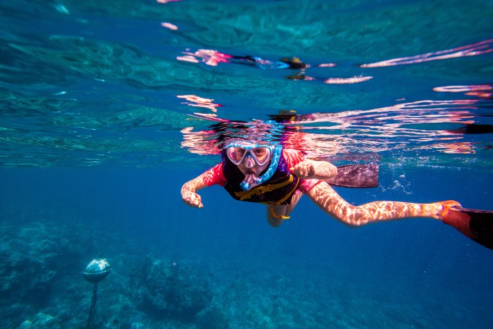 Person snorkeling underwater in clear blue ocean wearing mask and snorkel.