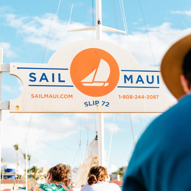 People standing near a Sail Maui sign on a sunny day.