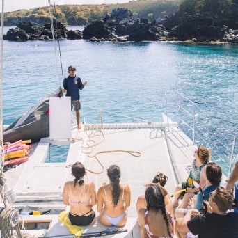 People on a boat near rocky shore, one person speaking to the group.