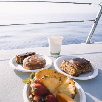 Plates of pastries and fruit on a table with ocean view in background.