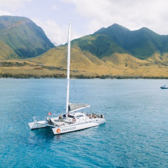 Catamaran sailing in blue water with green mountains in the background.