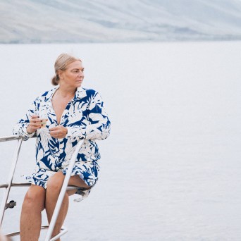 Person in blue floral shirt sitting on boat by calm water.