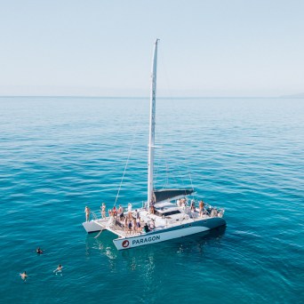 People relax on a sailboat named Paragon in clear blue water.