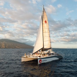 Sailboat on ocean with mountains and clouds in background.