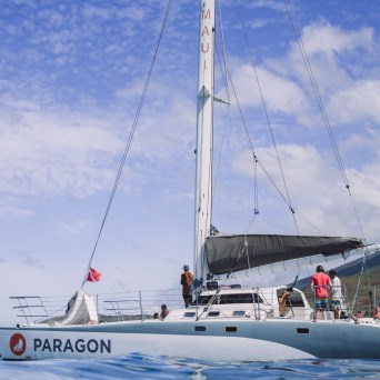 Sailboat with people on deck, mountains in background on a sunny day.