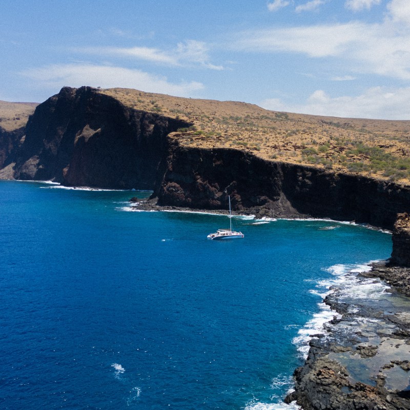 Cliffside view with a catamaran on blue ocean under partially cloudy sky.