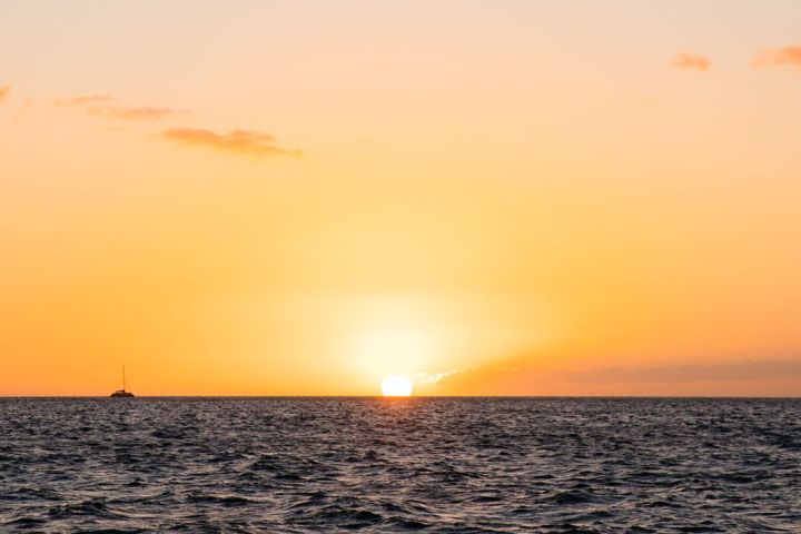 Sunset over the ocean with a distant boat silhouetted against the orange sky.