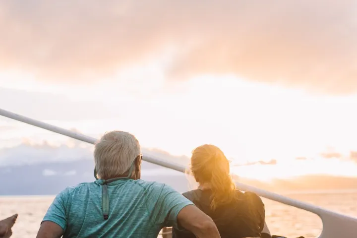 Two people sitting on a boat deck watching the sunset over the ocean.
