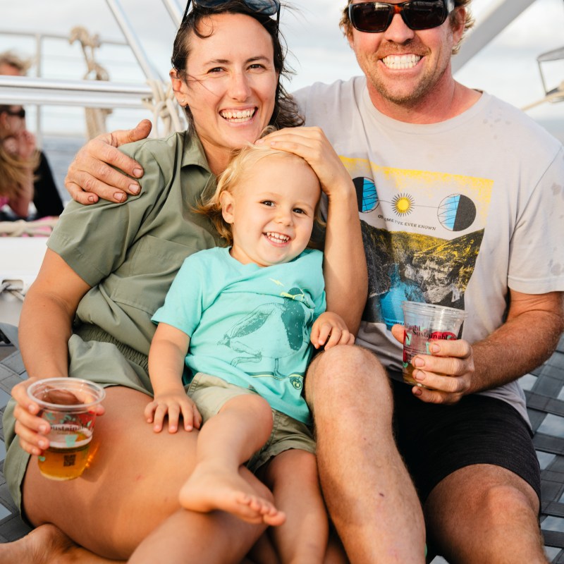 Smiling family on a boat, woman, man, and child holding drinks, sunny day.