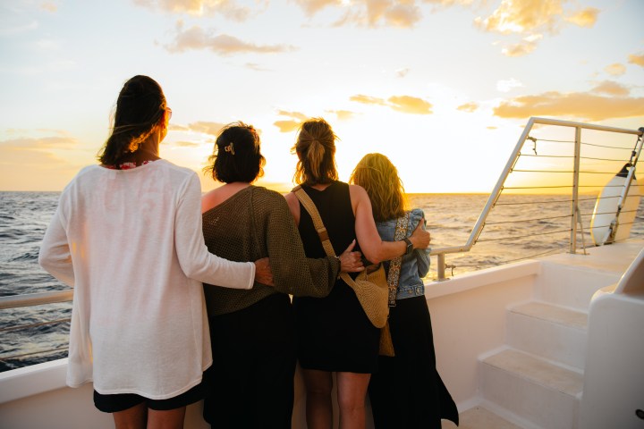 Four people embracing on a boat, watching the ocean sunset.