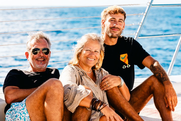 Three people sitting on a boat deck, smiling with the ocean in the background.