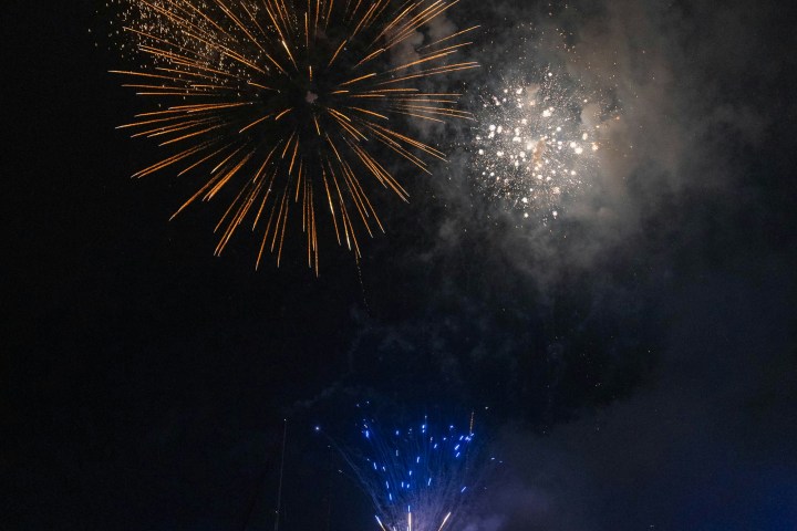 Fireworks explode over a body of water at night.