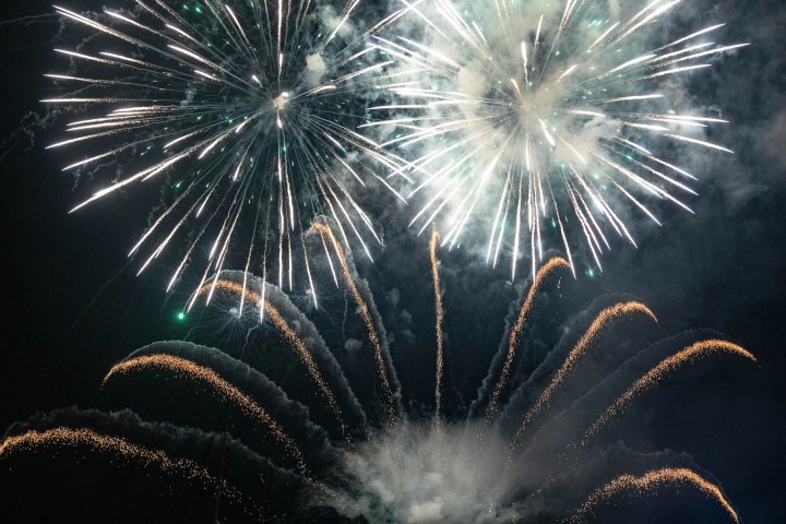 Bright fireworks exploding in the night sky over a calm body of water.