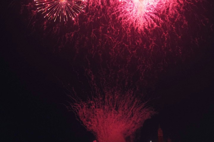 Red fireworks exploding over a dark waterfront at night.